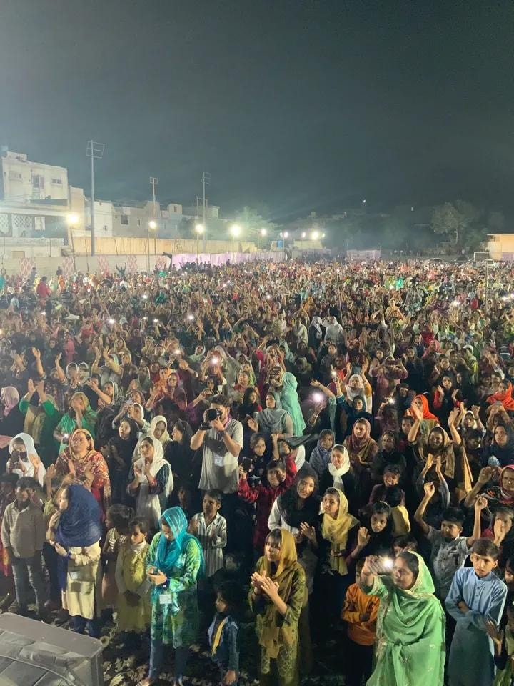 Large nighttime crusade crowd with raised hands and phone lights