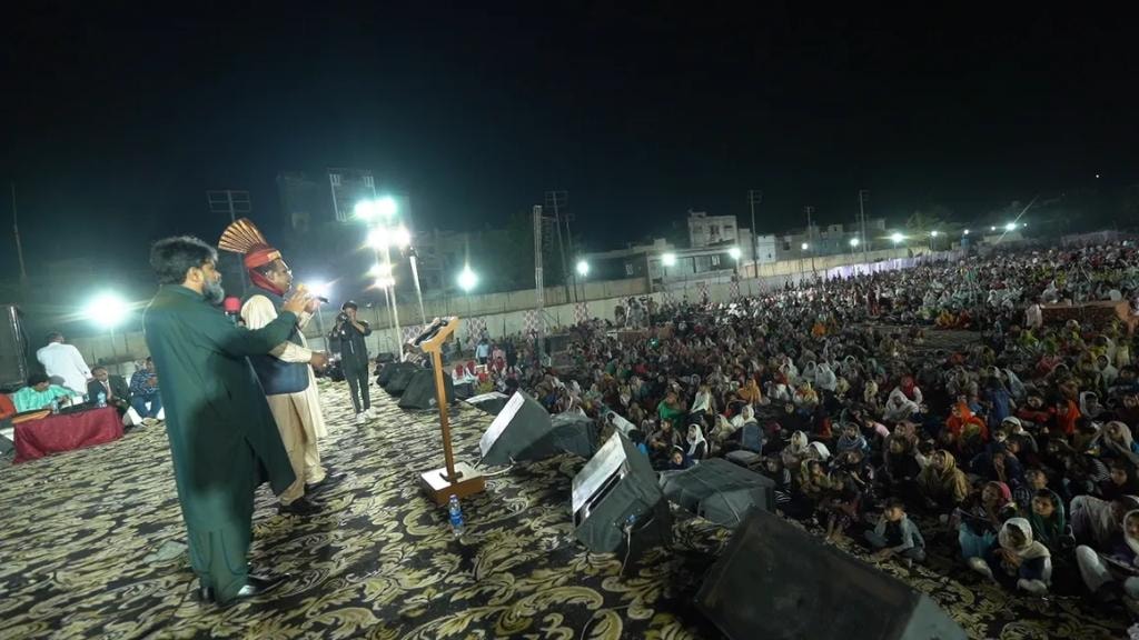 Pastor Larry Birgans preaching on stage to large outdoor crowd