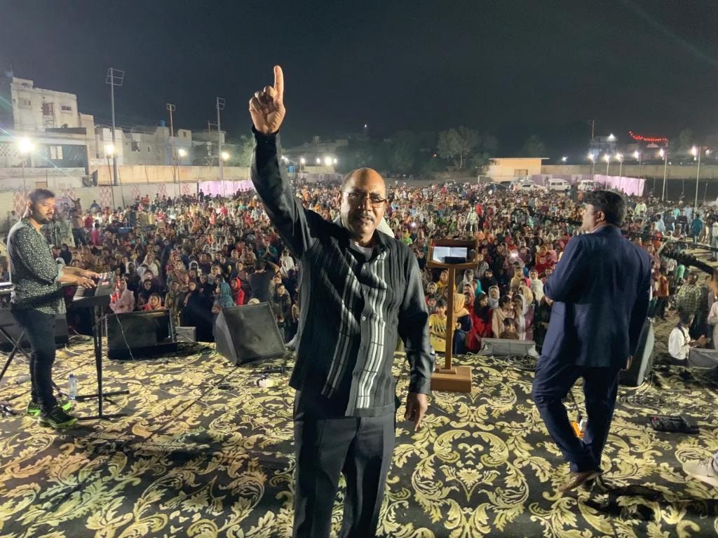 Pastor raising hand in praise before large crusade gathering